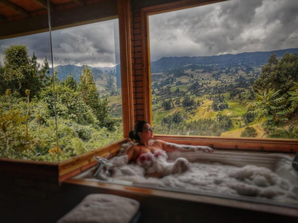 um homem numa banheira com uma grande janela em Cabaña Pacha Neusa em Cogua
