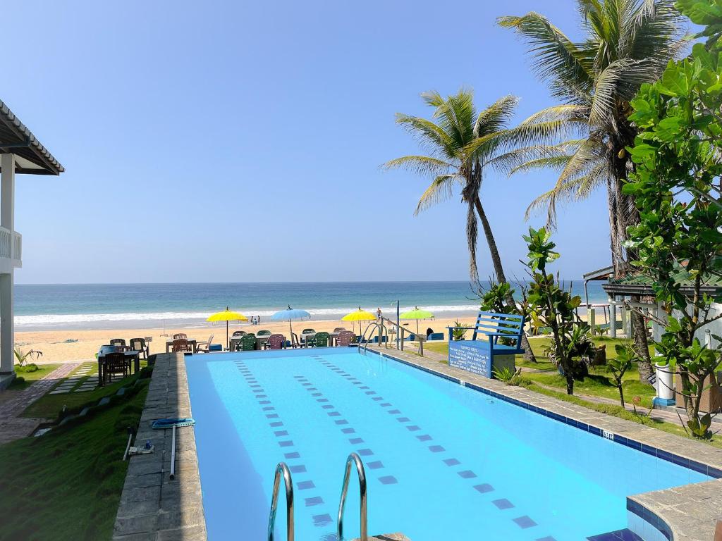 ein Schwimmbad mit Strand im Hintergrund in der Unterkunft Pearl Island Beach Hotel in Hikkaduwa