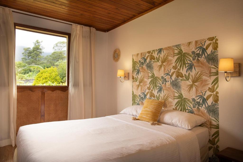 1 dormitorio con 1 cama blanca y ventana en Hôtel & Restaurant La Ferme Du Pommeau, en La Plaine-des-Palmistes