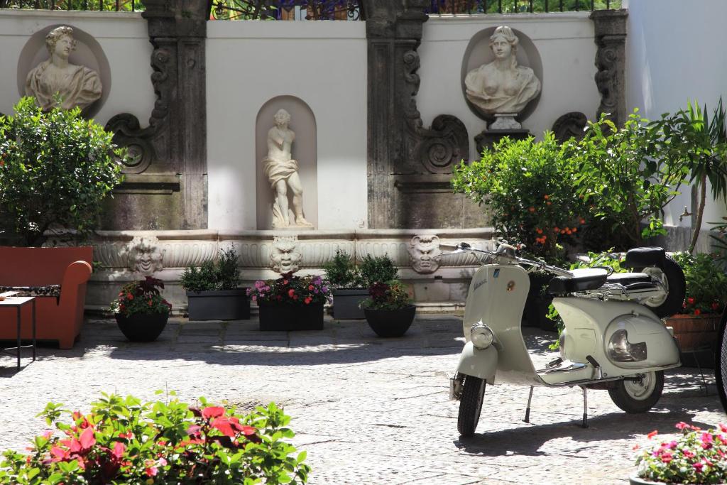 uma scooter estacionada em frente a um edifício com estátuas em Hotel Piazza Bellini & Apartments em Nápoles