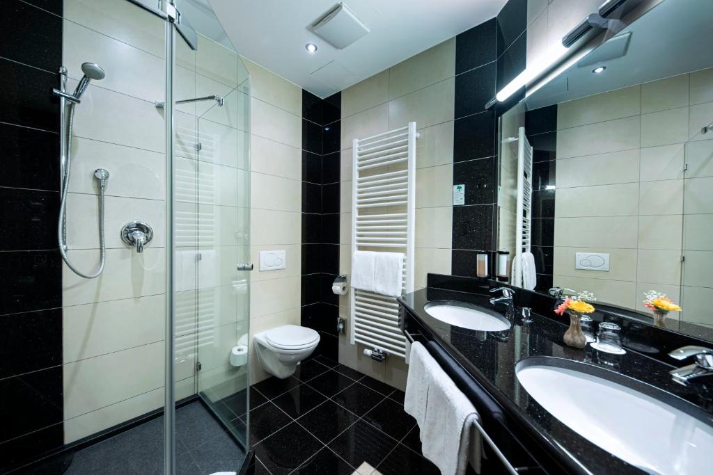 a bathroom with two sinks and a toilet and a glass shower at ACHAT Sternhotel Bonn in Bonn