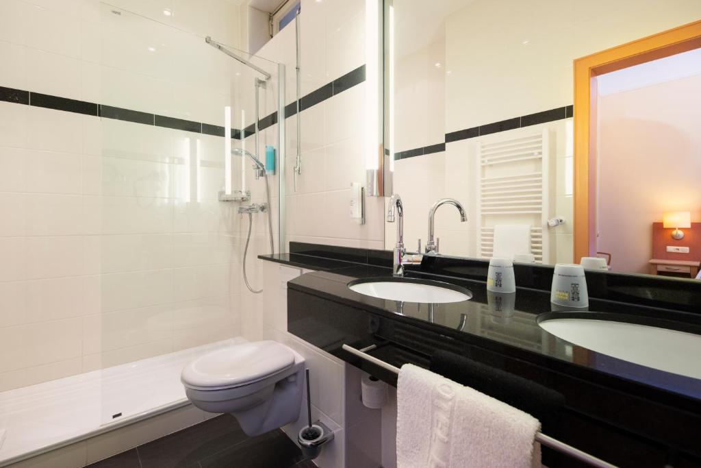a bathroom with two sinks and a toilet at ACHAT Sternhotel Bonn in Bonn