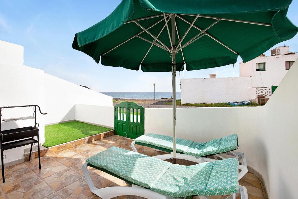 a patio with a green umbrella and chairs and a piano at Mar de Lava Sunrise Fuerteventura in Pozo Negro