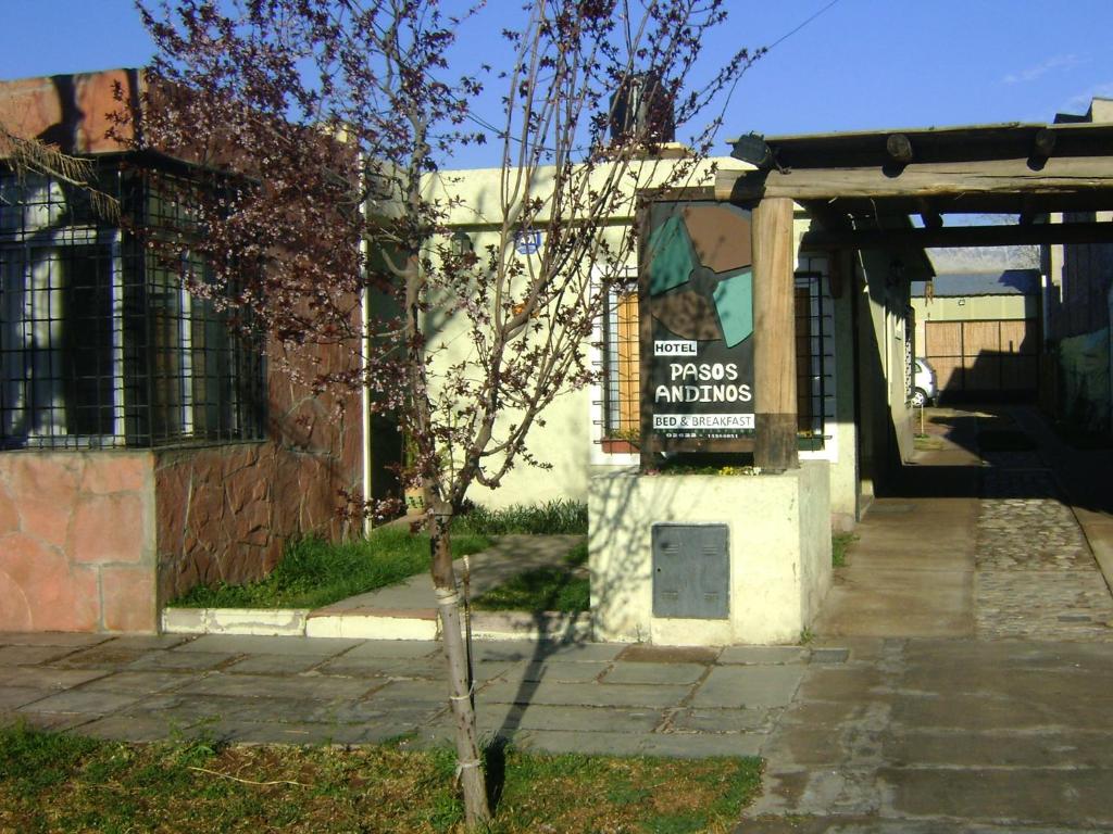 Un árbol delante de un edificio con un cartel. en Pasos Andinos B&B en Eugenio Bustos