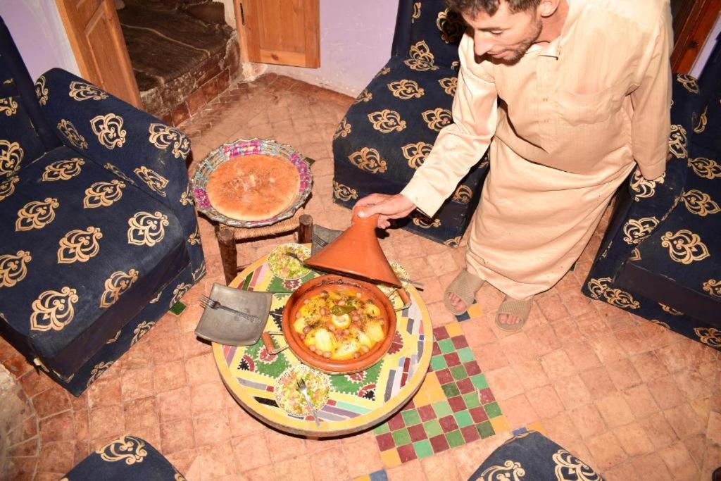 Ein Mann steht neben einem Tisch mit einem Topf Essen. in der Unterkunft Chez Hassan Dar Bejmate in Tacheddirt