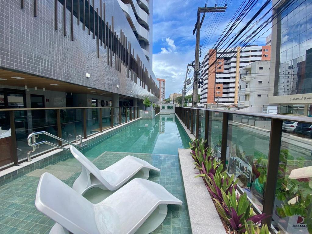 un edificio con piscina y 2 sillas blancas en Studio Design - apto com varanda e lazer completo na Ponta Verde, en Maceió