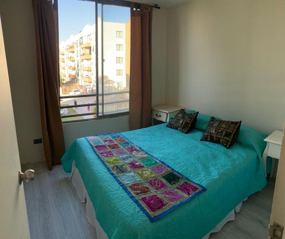 ein Schlafzimmer mit einem Bett mit blauer Decke und einem Fenster in der Unterkunft DEPTOS LA SERENA in Coquimbo