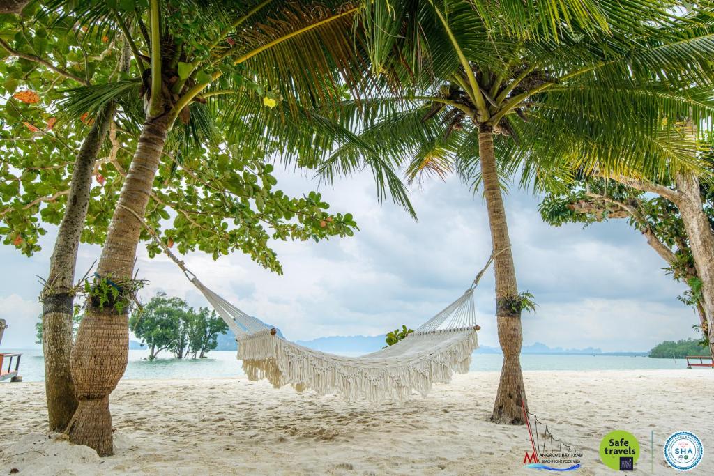a hammock between two palm trees on a beach at Mangrovebay Krabi Beachfront Pool Villa in Ban Nai Sa