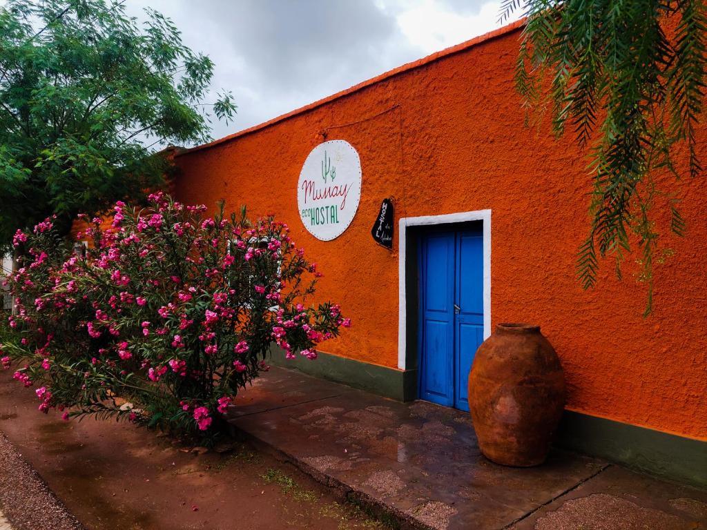 Munay EcoHostal - Cabañas de Adobe في تينوغاستا: مبنى برتقالي مع باب أزرق وورود