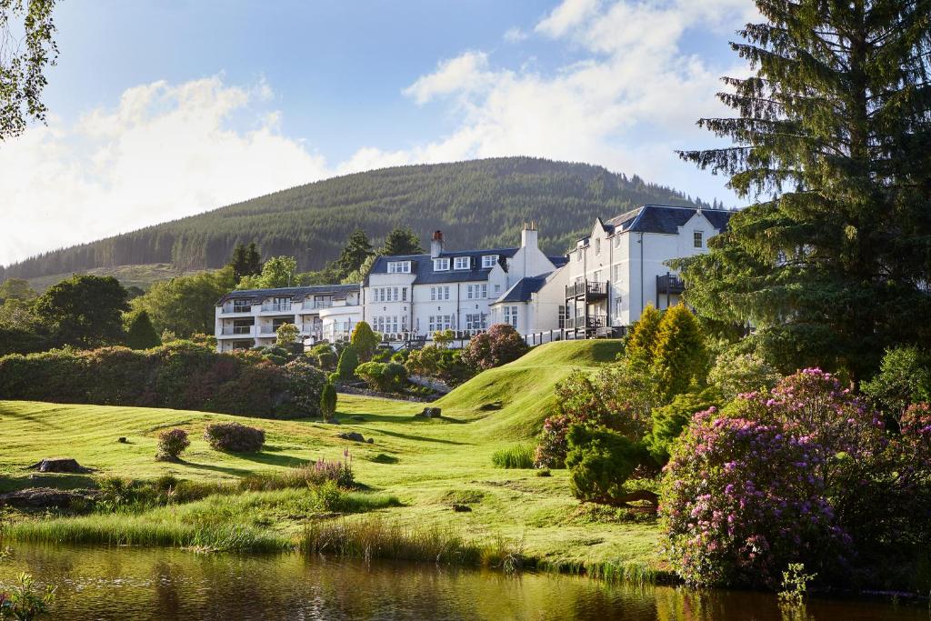 a large house on a hill next to a body of water at Macdonald Forest Hills Hotel & Spa in Aberfoyle