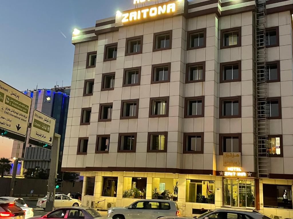 un grand bâtiment avec des voitures garées devant lui dans l'établissement Hotel Zaitona, à Erbil