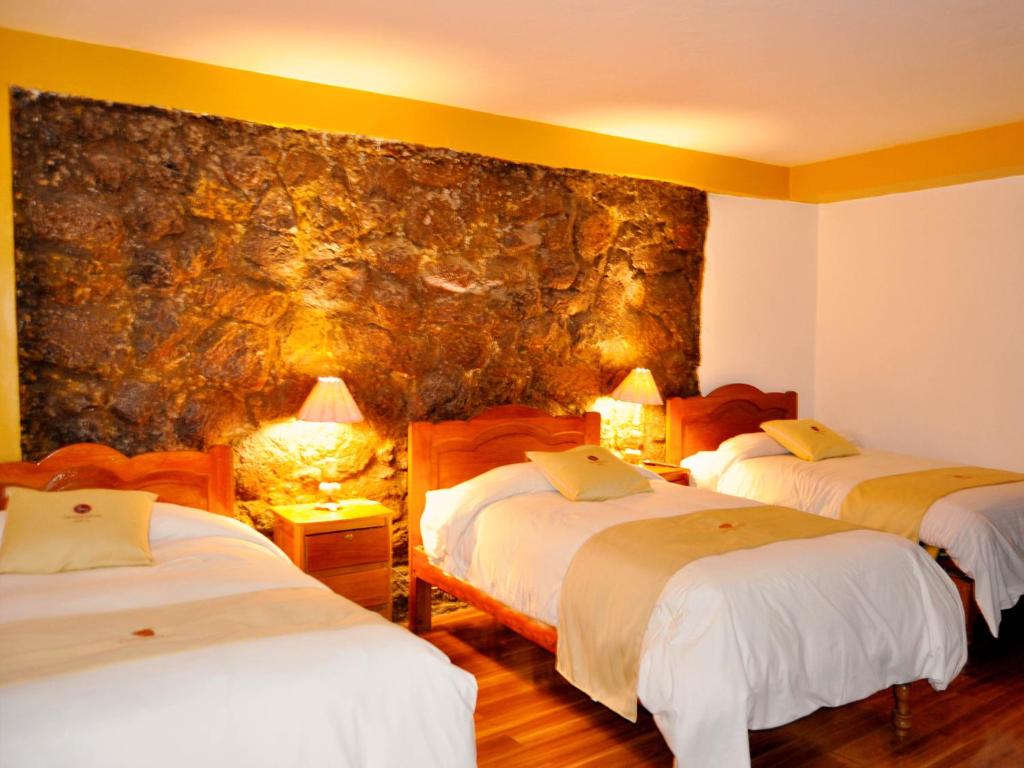 Habitación de hotel con 3 camas y pared de piedra. en Hotel Choquequirao, en Cusco