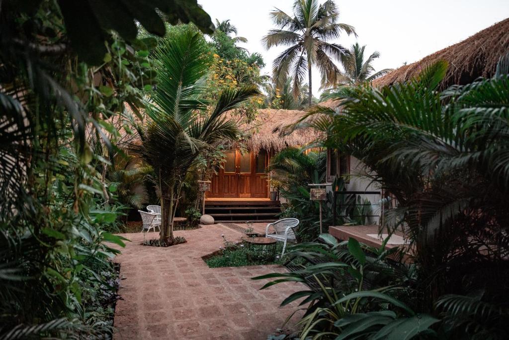 a garden with palm trees and a house with a patio at Anahata Retreat Sea Front Resort Ashvem in Mandrem