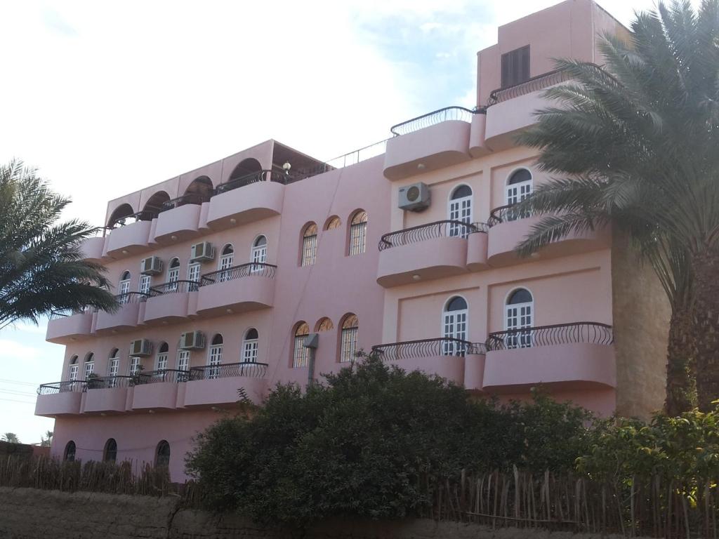 a pink building with balconies and palm trees at Amenophis Hotel in Luxor