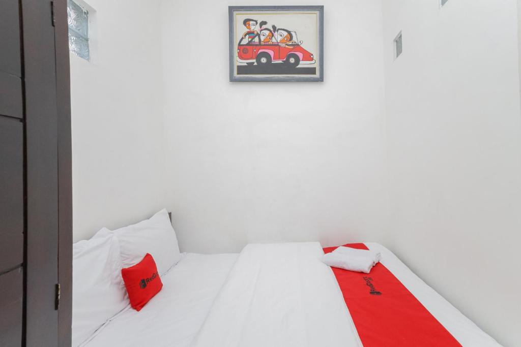 un letto bianco con cuscini rossi e una foto di un'auto di RedDoorz Syariah near Universitas Jember a Jember
