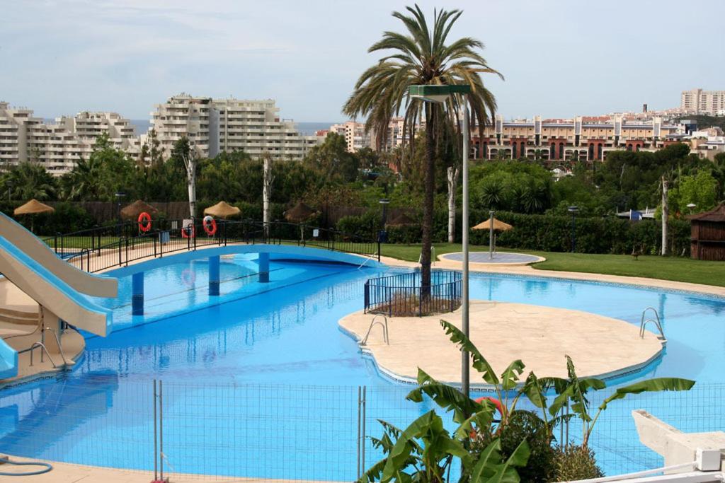 a large blue swimming pool with a palm tree and buildings at Apartamentos Minerva Jupiter in Benalmádena