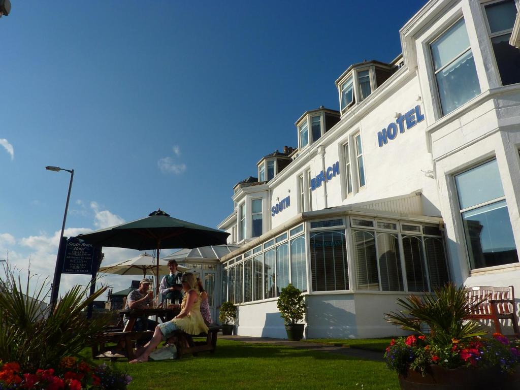 a woman sitting under an umbrella in front of a hotel at South Beach Hotel in Troon