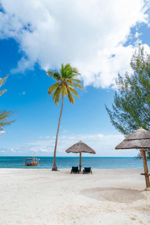 a beach with two umbrellas and a palm tree at The Residence Zanzibar in Kizimkazi