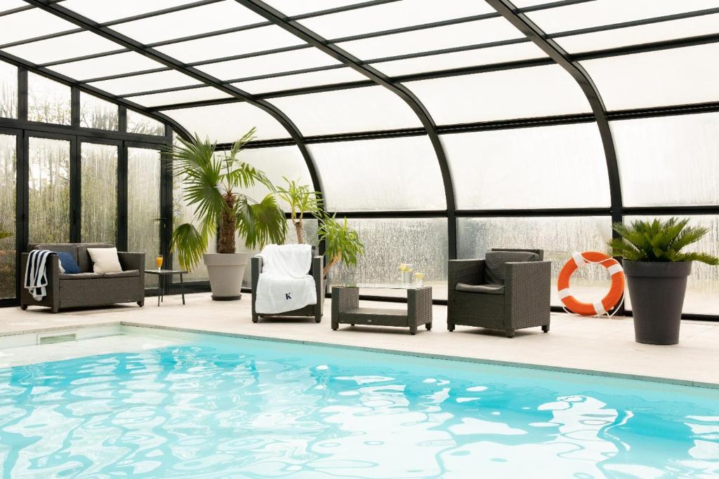 a swimming pool in a conservatory with chairs and a table at Kyriad Prestige Residence & Spa Cabourg-Dives-sur-Mer in Dives-sur-Mer