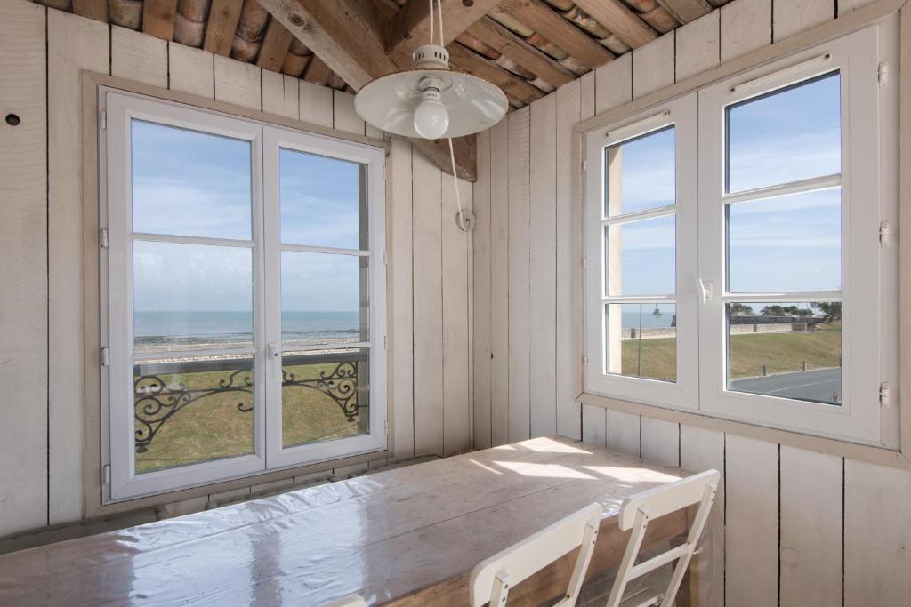 a dining room with a table and two windows at Appartement Neptune in Saint-Martin-de-Ré