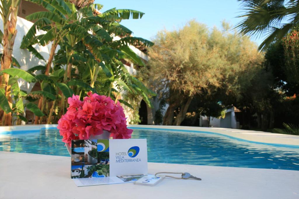 una mesa con un ramo de flores rosas y una tarjeta en Hotel Villa Mediterranea, en Marina di Noto