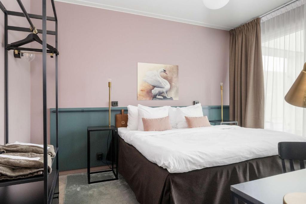 um quarto com uma cama com lençóis brancos e paredes cor-de-rosa em Best Western Plus Hus 57 em Ängelholm