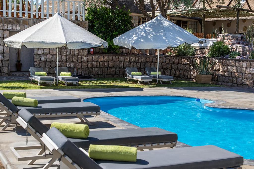 a swimming pool with chaise lounge chairs and umbrellas at Elegant Desert Lodge in Sesriem