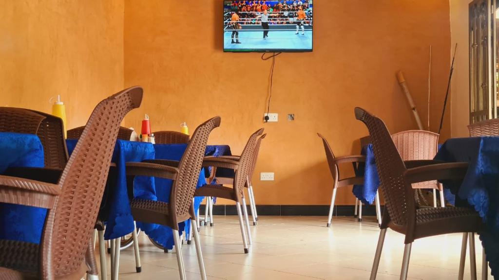 een eetkamer met blauwe tafels en stoelen en een tv bij Haber Motel Enterprise Ltd in Entebbe
