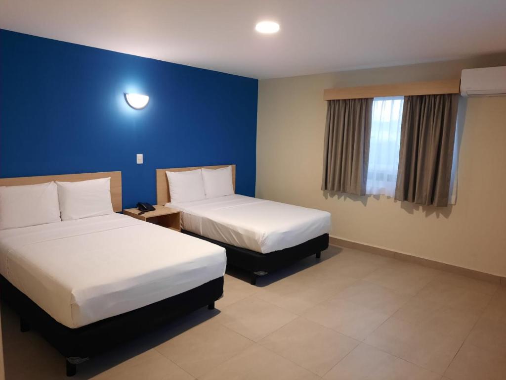 Habitación de hotel con 2 camas y pared azul en CHN Hotel Monterrey Santa Fe en Monterrey