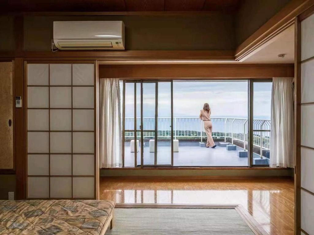 Izu One Club - Vacation STAY 10141v في Futo: امرأة تقف في غرفة مع نافذة كبيرة