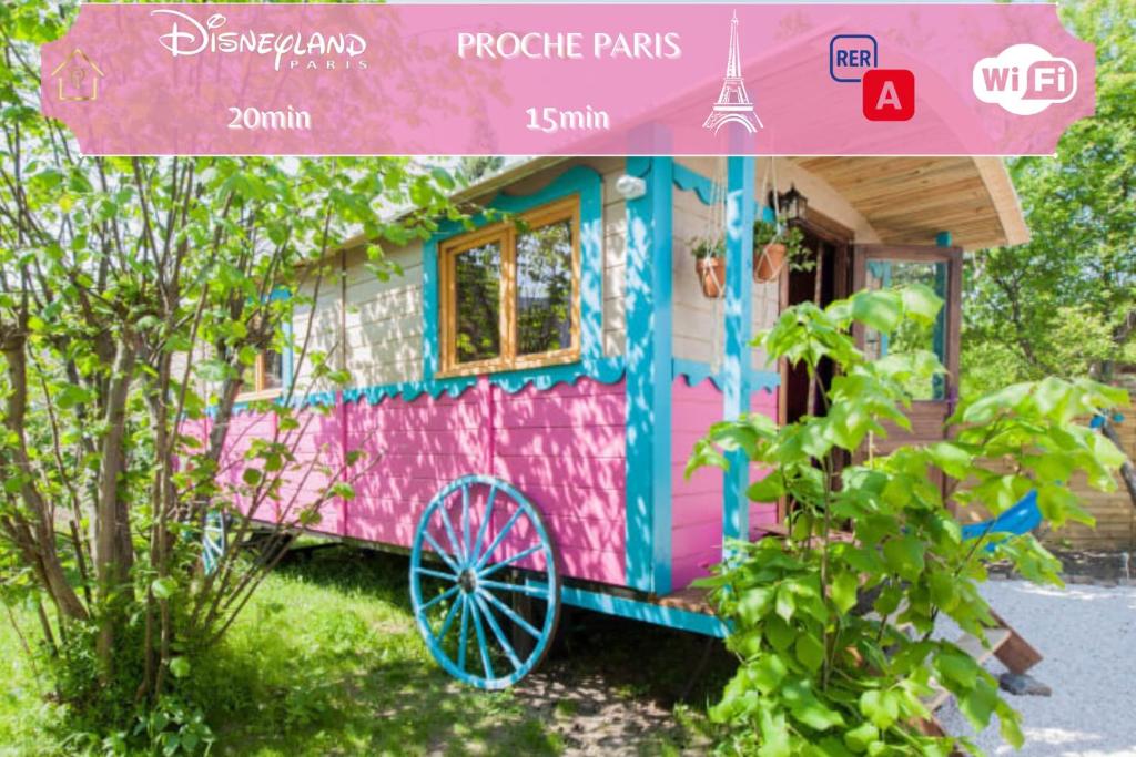 una casa rosa y colorida con una rueda delante en Roulotte Insolite avec terrasse proche Paris, en Noisy-le-Grand