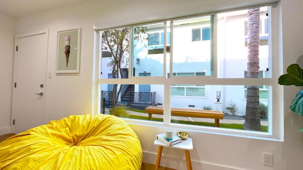 ein Wohnzimmer mit einem großen Fenster und einer gelben Ottomane in der Unterkunft Kingsley Courtyard Apartment in Los Angeles