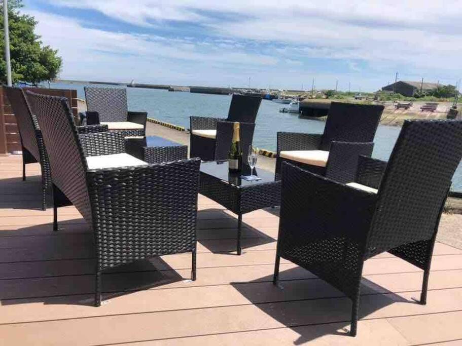 eine Reihe von Stühlen und Tischen auf einer Terrasse mit Blick auf das Wasser in der Unterkunft Pier39 Uchiumi Cozy house located in front of the sea and harbor! in Miyazaki