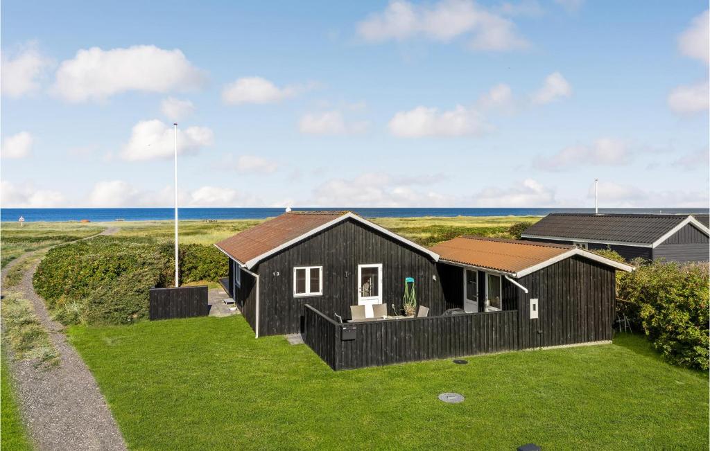 a black house on a lawn with the ocean in the background at Lovely Home In Lgstr With Kitchen in Løgstør