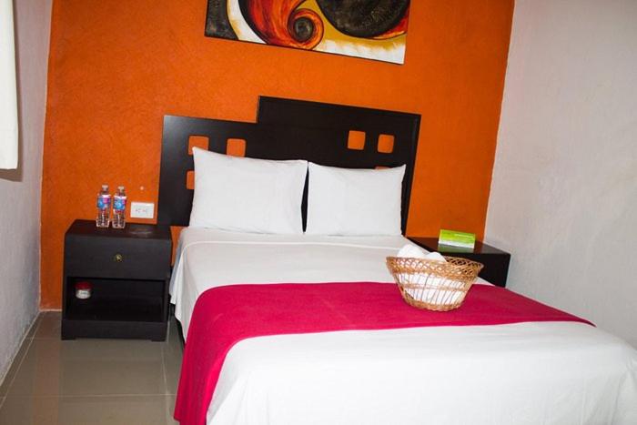 - une chambre avec un grand lit blanc et un mur orange dans l'établissement Rosvel, à Palenque