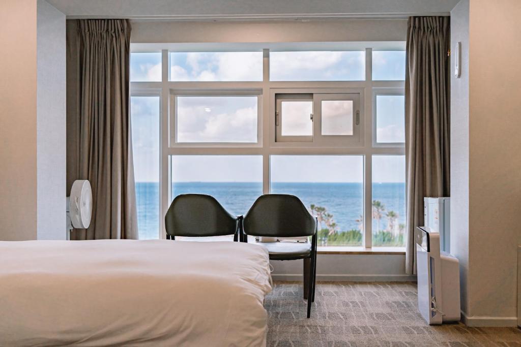 um quarto com uma cama e duas cadeiras em frente a uma janela em Cocoon Hotel em Jeju