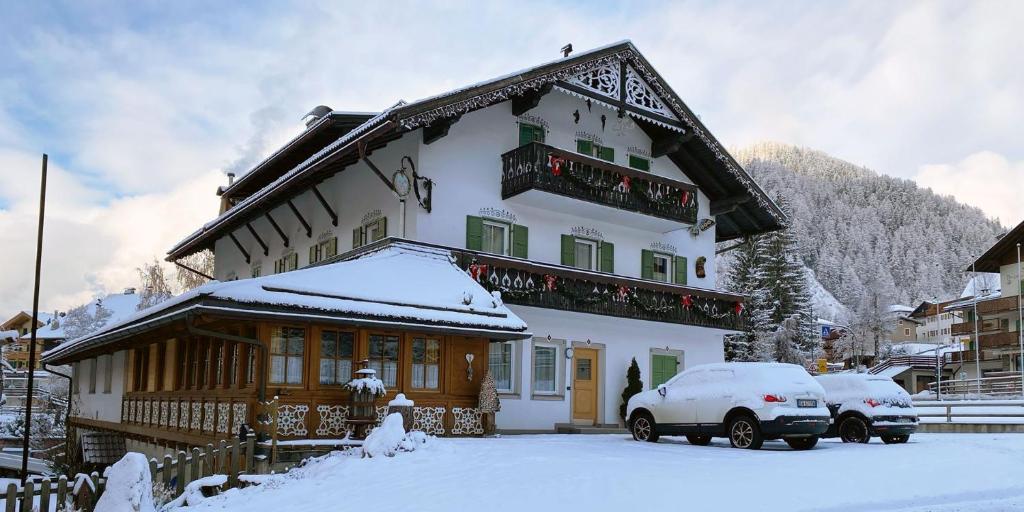 a snow covered house with two cars parked in front of it at Appartamenti Stefan in Campitello di Fassa