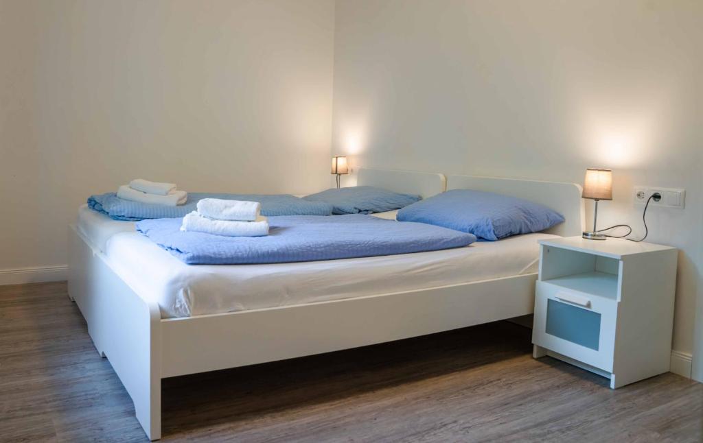 a white bed with blue pillows and a night stand at Appartementhaus Brunsholm in Esgrus