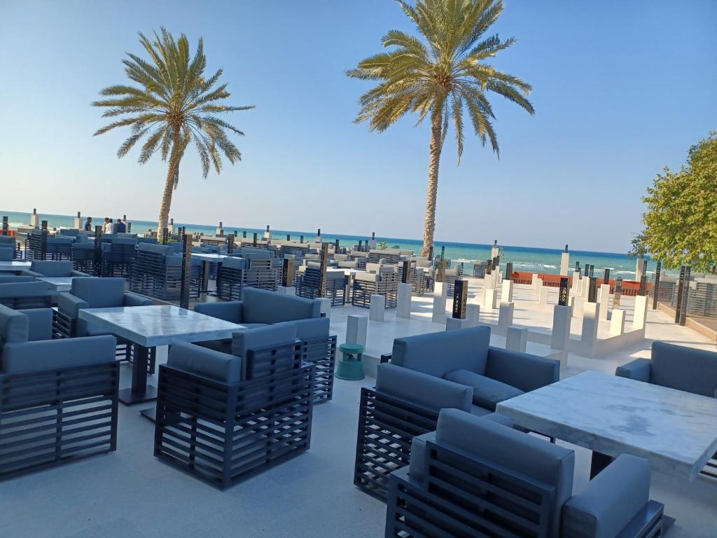 een strand met tafels en stoelen en palmbomen bij Al Qurum Resort in Muscat