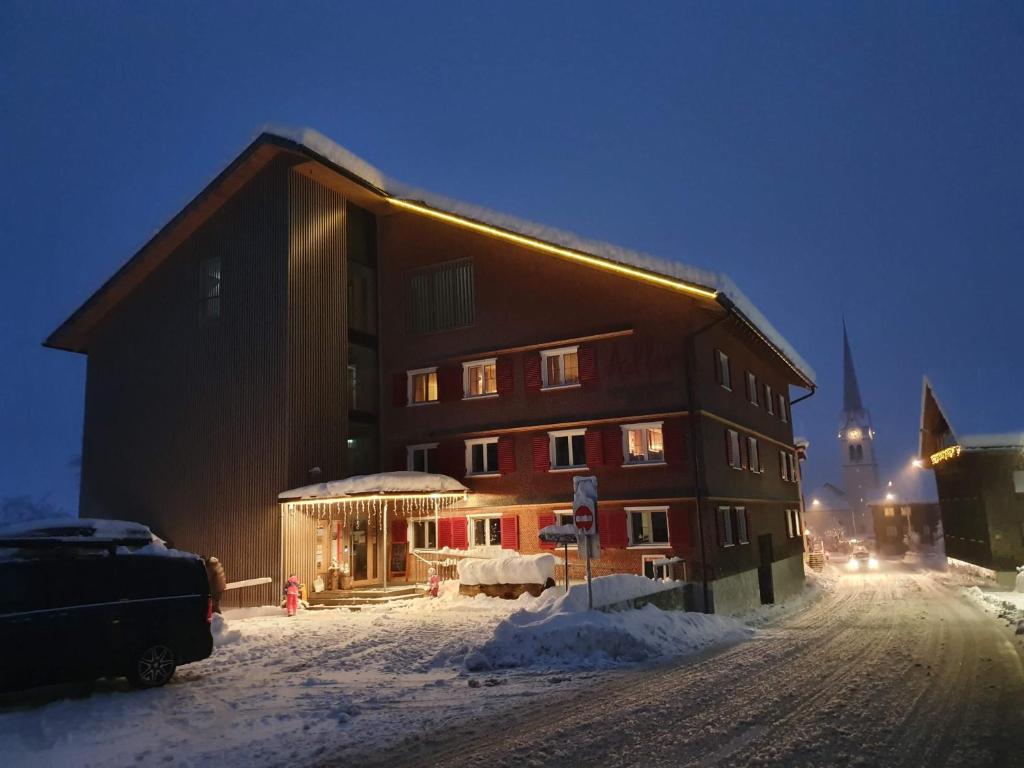 ein Gebäude im Schnee mit einer Kirche im Hintergrund in der Unterkunft Hotel Gasthof Adler in Lingenau