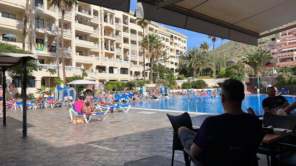 a group of people sitting in chairs at a swimming pool at Castle Harbour Home in Los Cristianos