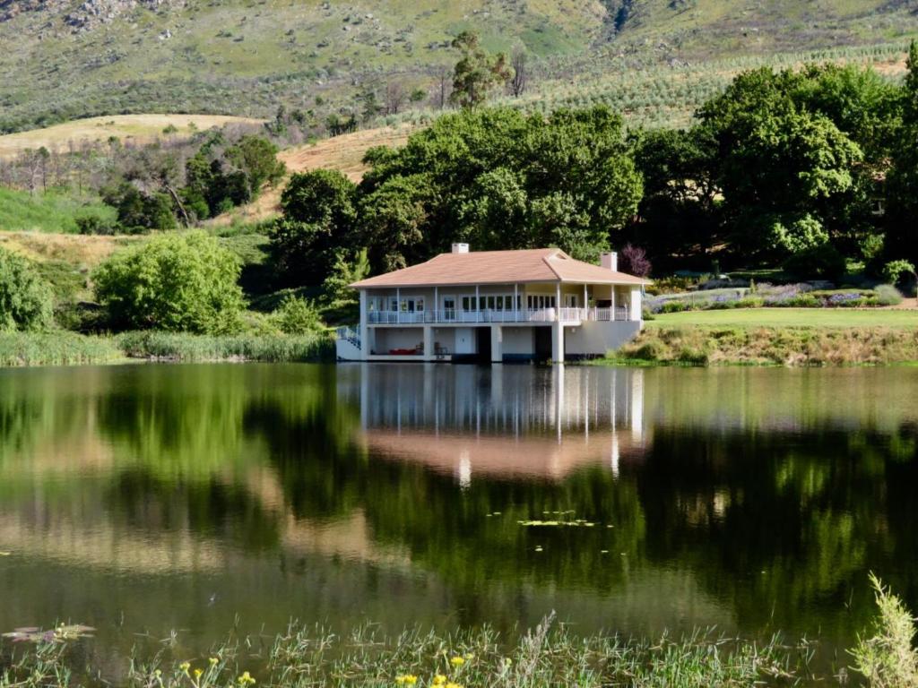 a large house on a lake with mountains in the background at The Boathouse at Oakhurst Olives in Tulbagh