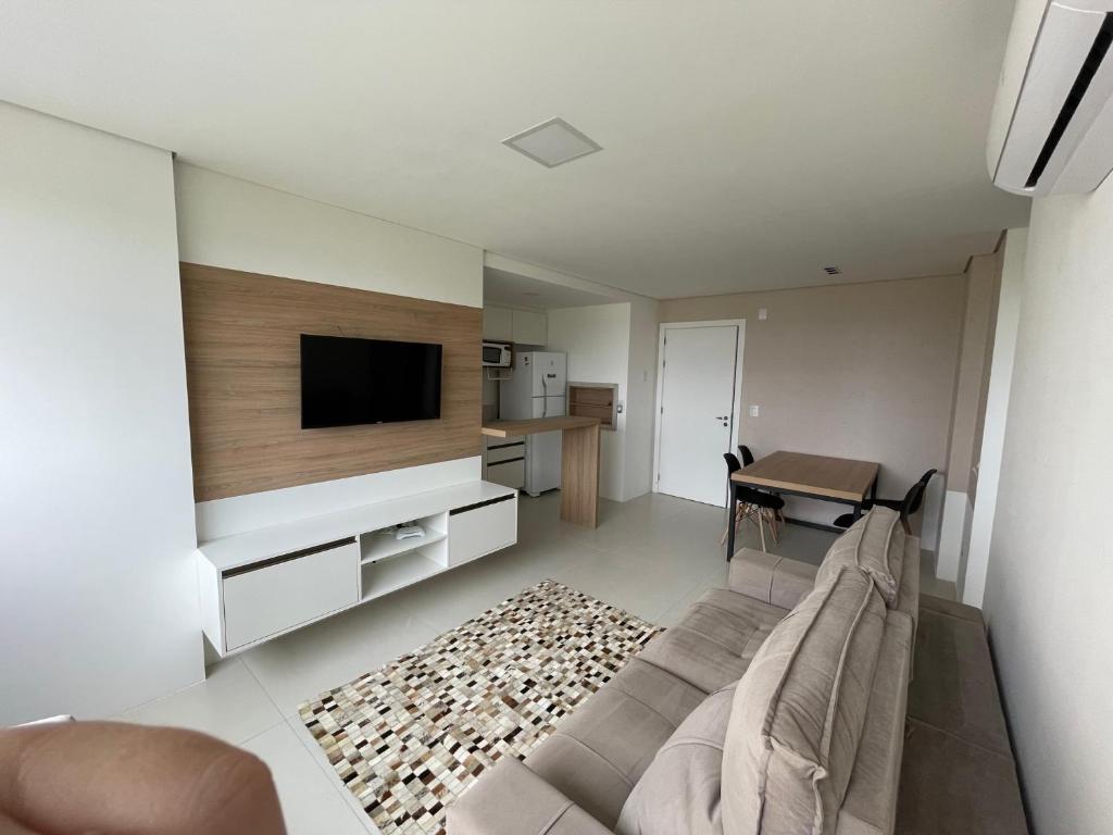 a living room with a couch and a tv and a table at Apartamento 2 quartos c/ Piscina 3 Ar-condicionado in Torres