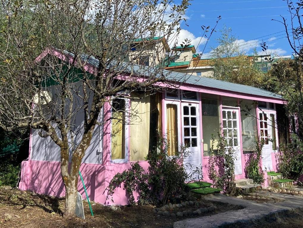 ein rosa und weißes Haus mit einem Baum in der Unterkunft SAIRRA - Hotel & Restaurant in Manali