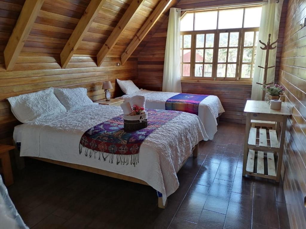 two beds in a room with wooden walls and windows at La Cabaña de Mari in Oxapampa