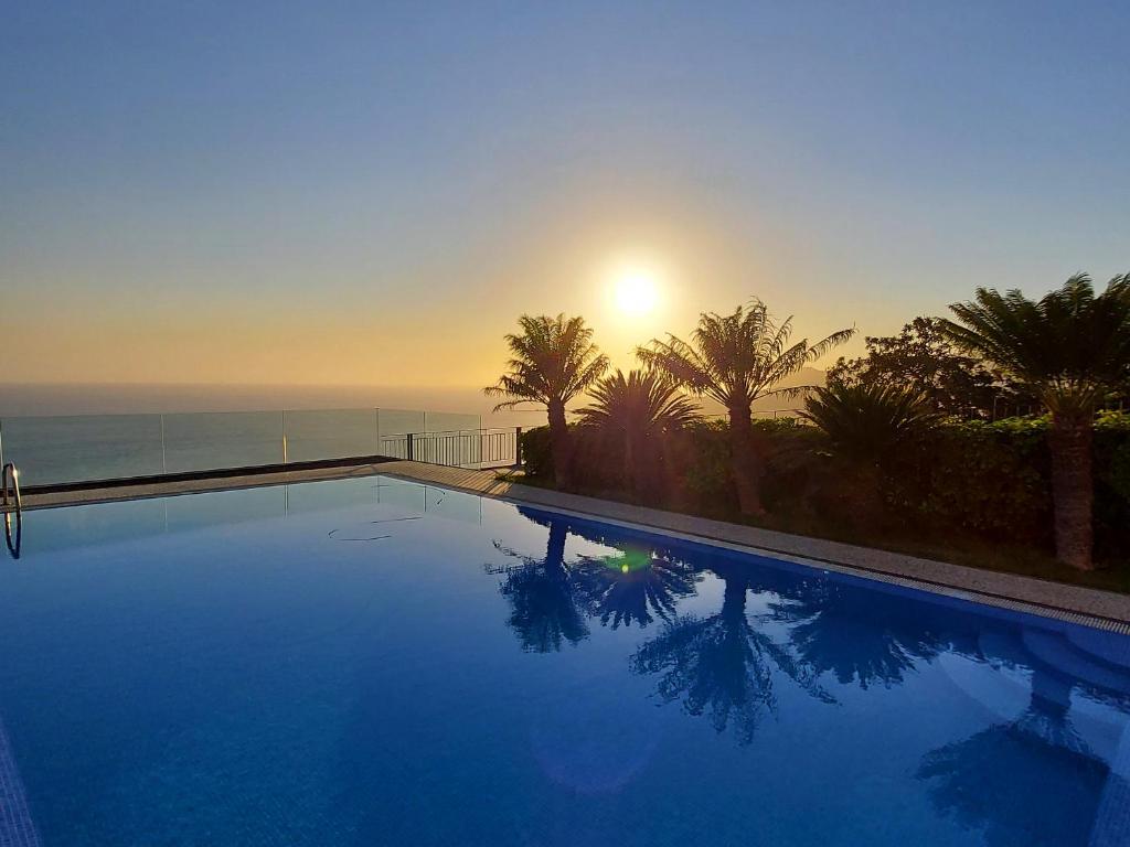 a swimming pool with the sun setting over the ocean at Neves by BCA Villas in São Gonçalo