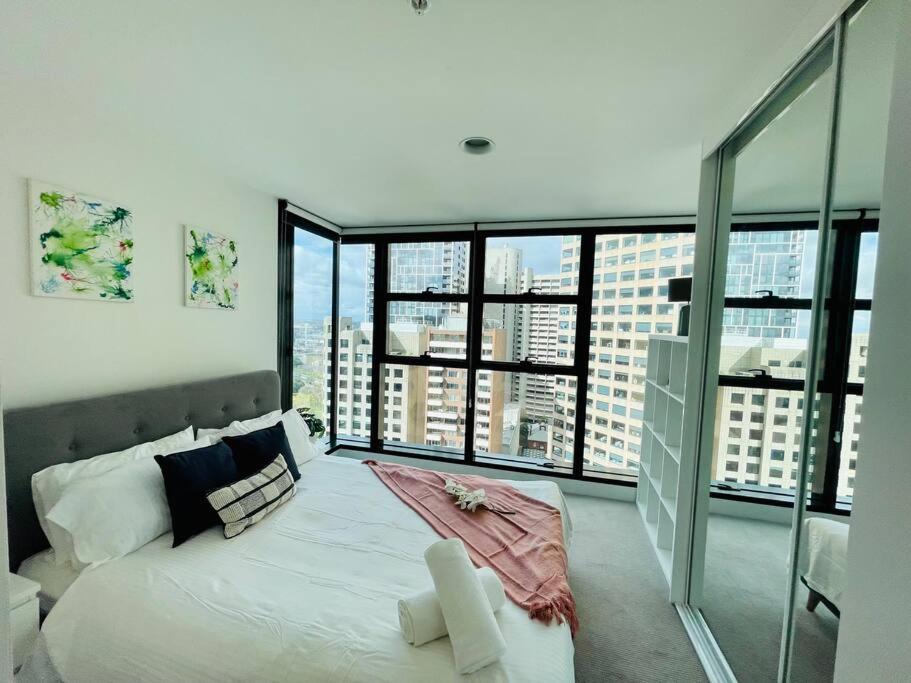 1 dormitorio con 1 cama blanca grande y ventanas grandes en Cozy unit close to Parliament w/Amazing City Views en Melbourne