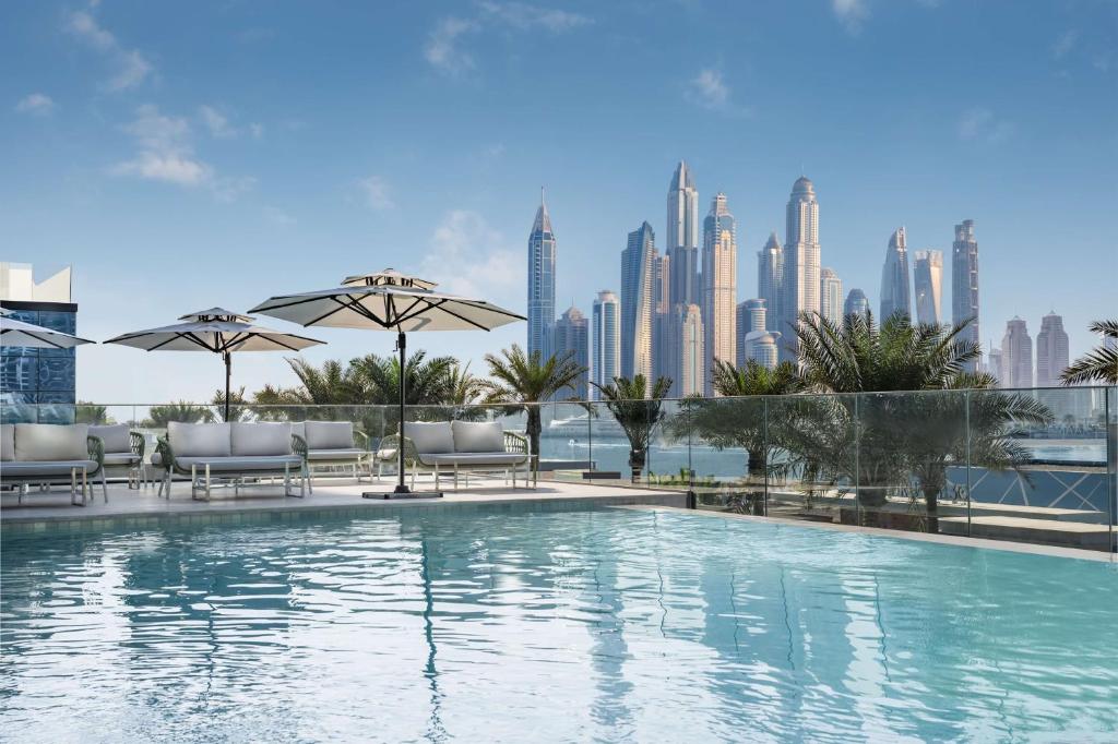 a pool with chairs and umbrellas and a city skyline at Radisson Beach Resort Palm Jumeirah in Dubai