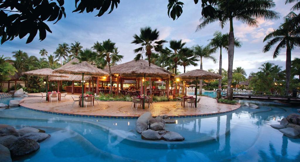 a pool at a resort with tables and umbrellas at Outrigger Fiji Beach Resort in Korotogo