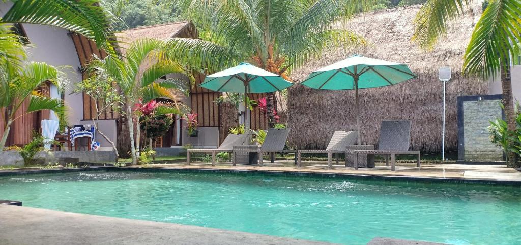 a swimming pool with chairs and umbrellas in front of a building at Bale Lumbung Bungalows in Nusa Penida
